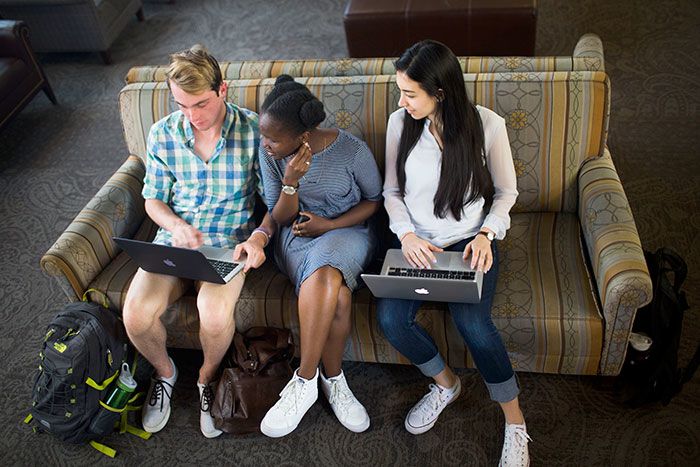 three students looking at a laptop while sitting on couch in Dobbs Hall